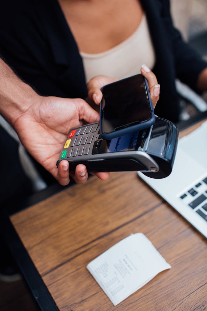 Hands making a contactless mobile payment with a smartphone at a terminal.